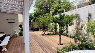 חצר גדולה עם דק עץ בהיר ופרגולה לבנה